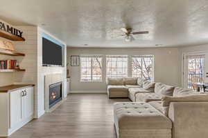 Living room featuring ceiling fan, a textured ceiling, a fireplace, and light wood-type flooring