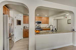 Kitchen featuring light stone counters, sink, light wood-type flooring, and appliances with stainless steel finishes