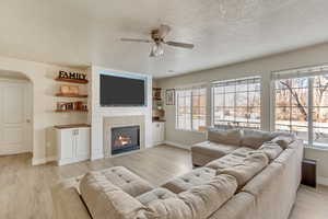 Living room with ceiling fan, a fireplace, light hardwood / wood-style floors, and a textured ceiling