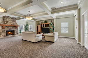 Carpeted living room featuring coffered ceiling, a stone fireplace, a textured ceiling, ornamental molding, and beam ceiling