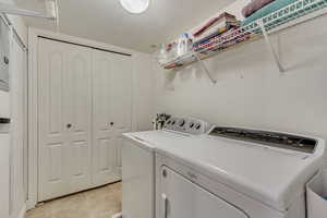 Laundry room with light tile patterned flooring, washing machine and dryer, and a textured ceiling