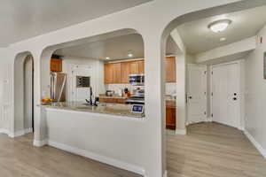 Entrance on the right side of the Photo: Kitchen featuring sink, light wood-type flooring, stainless steel appliances, and light stone countertops