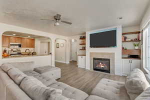 Living room featuring a textured ceiling, a tile fireplace, ceiling fan, and light wood-type flooring