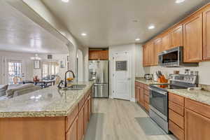 Kitchen with appliances with stainless steel finishes, a kitchen island with sink, sink, and light wood-type flooring