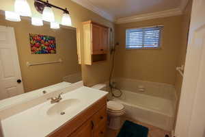 Bathroom with a tub to relax in, vanity, toilet, and crown molding