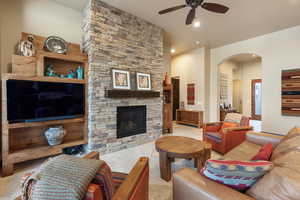 Tiled living room with a stone fireplace and ceiling fan