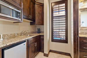 Kitchen featuring sink, dishwasher, dark brown cabinetry, light stone countertops, and light tile patterned flooring