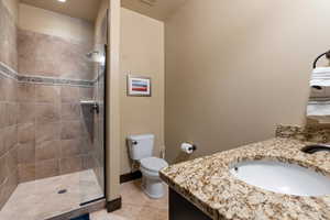 Bathroom with a shower with door, vanity, tile patterned floors, and toilet