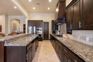 Kitchen featuring sink, appliances with stainless steel finishes, a kitchen island with sink, premium range hood, and decorative backsplash