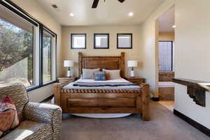 Carpeted bedroom featuring multiple windows, ceiling fan, and ensuite bath