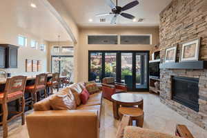 Living room featuring ceiling fan, a wealth of natural light, a stone fireplace, and light tile patterned floors