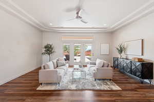 Living room with a tray ceiling, dark wood-type flooring, and ceiling fan