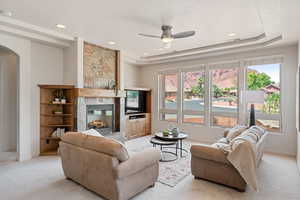 Living room featuring a tray ceiling, a fireplace, light carpet, and a wealth of natural light