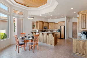 Kitchen with a kitchen bar, decorative light fixtures, paneled built in refrigerator, a tray ceiling, and light stone countertops