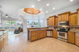 Kitchen with sink, stone counters, appliances with stainless steel finishes, hanging light fixtures, and a raised ceiling