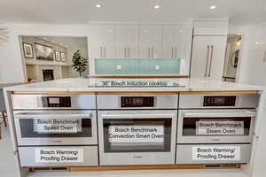 Kitchen featuring stainless steel oven, black electric stovetop, white cabinets, and light stone counters