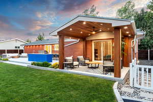 Back house at dusk featuring ceiling fan, an outdoor hangout area, a patio, and a lawn