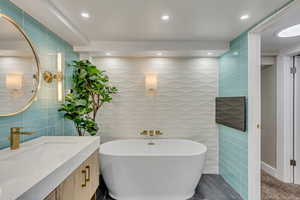 Bathroom featuring vanity, tile walls, and a tub to relax in