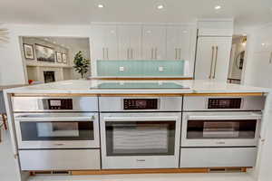 Kitchen with white cabinetry, tasteful backsplash, black electric cooktop, and light stone counters