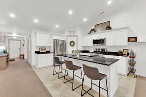 Kitchen featuring white cabinetry, stainless steel appliances, an island with sink, light tile patterned flooring, and vaulted ceiling