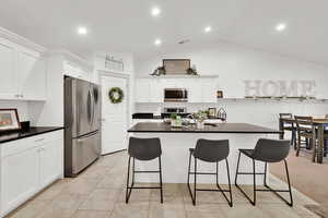 Kitchen with sink, appliances with stainless steel finishes, a kitchen breakfast bar, white cabinets, and vaulted ceiling