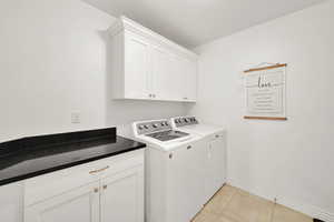 Washroom with light tile patterned floors, cabinets, and washing machine and clothes dryer