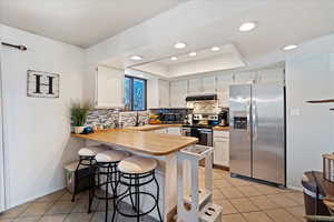 Kitchen featuring sink, appliances with stainless steel finishes, white cabinets, a kitchen bar, and kitchen peninsula