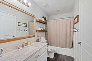 Full bathroom featuring toilet, a textured ceiling, vanity, shower / bath combo with shower curtain, and hardwood / wood-style floors