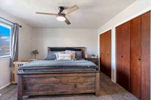 Bedroom with a textured ceiling, ceiling fan, and dark colored carpet