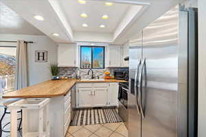 Kitchen with sink, light tile patterned floors, appliances with stainless steel finishes, white cabinetry, and wood counters