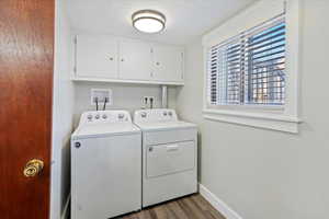 Clothes washing area featuring cabinets, washing machine and dryer, dark hardwood / wood-style floors, and a textured ceiling