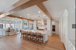 Kitchen featuring white cabinetry, a breakfast bar area, hanging light fixtures, beam ceiling, and a spacious island