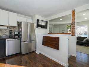 Kitchen with dark wood-type flooring, white cabinetry, a textured ceiling, appliances with stainless steel finishes, and decorative backsplash