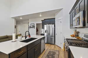 Kitchen with an island with sink, appliances with stainless steel finishes, sink, and light laminate / wood-style floors