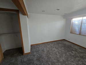 Unfurnished bedroom featuring a closet, a textured ceiling, and dark colored carpet