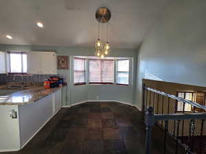 Kitchen with decorative light fixtures, white cabinetry, sink, backsplash, and kitchen peninsula