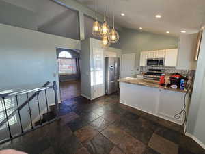 Kitchen with high vaulted ceiling, hanging light fixtures, white cabinets, stainless steel appliances, and backsplash