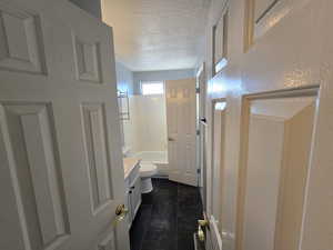 Full bathroom with washtub / shower combination, tile patterned flooring, vanity, a textured ceiling, and toilet