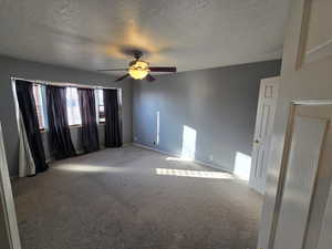 Unfurnished room featuring a textured ceiling, carpet floors, and ceiling fan