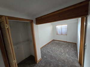 Unfurnished bedroom with a textured ceiling, a closet, and dark colored carpet