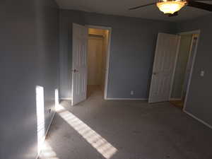 Unfurnished bedroom with a walk in closet, light colored carpet, ceiling fan, and a closet