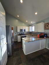 Kitchen with lofted ceiling, sink, appliances with stainless steel finishes, kitchen peninsula, and dark stone counters