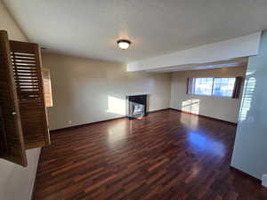 Unfurnished living room featuring a textured ceiling and dark hardwood / wood-style flooring