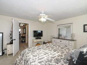 Bedroom featuring ceiling fan, light carpet, and a textured ceiling