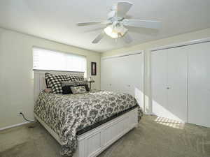 Bedroom with multiple closets, ceiling fan, and light carpet