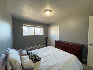 Carpeted bedroom with a baseboard heating unit and a textured ceiling