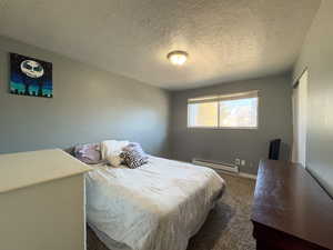 Bedroom with a baseboard radiator, a textured ceiling, and dark carpet