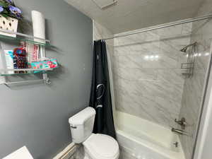 Bathroom with shower / bathtub combination with curtain, a textured ceiling, and toilet