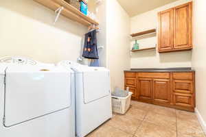 Laundry room with cabinets, washing machine and dryer, and light tile patterned flooring