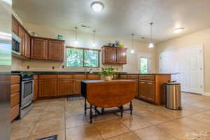 Kitchen with appliances with stainless steel finishes, decorative light fixtures, sink, and light tile patterned floors